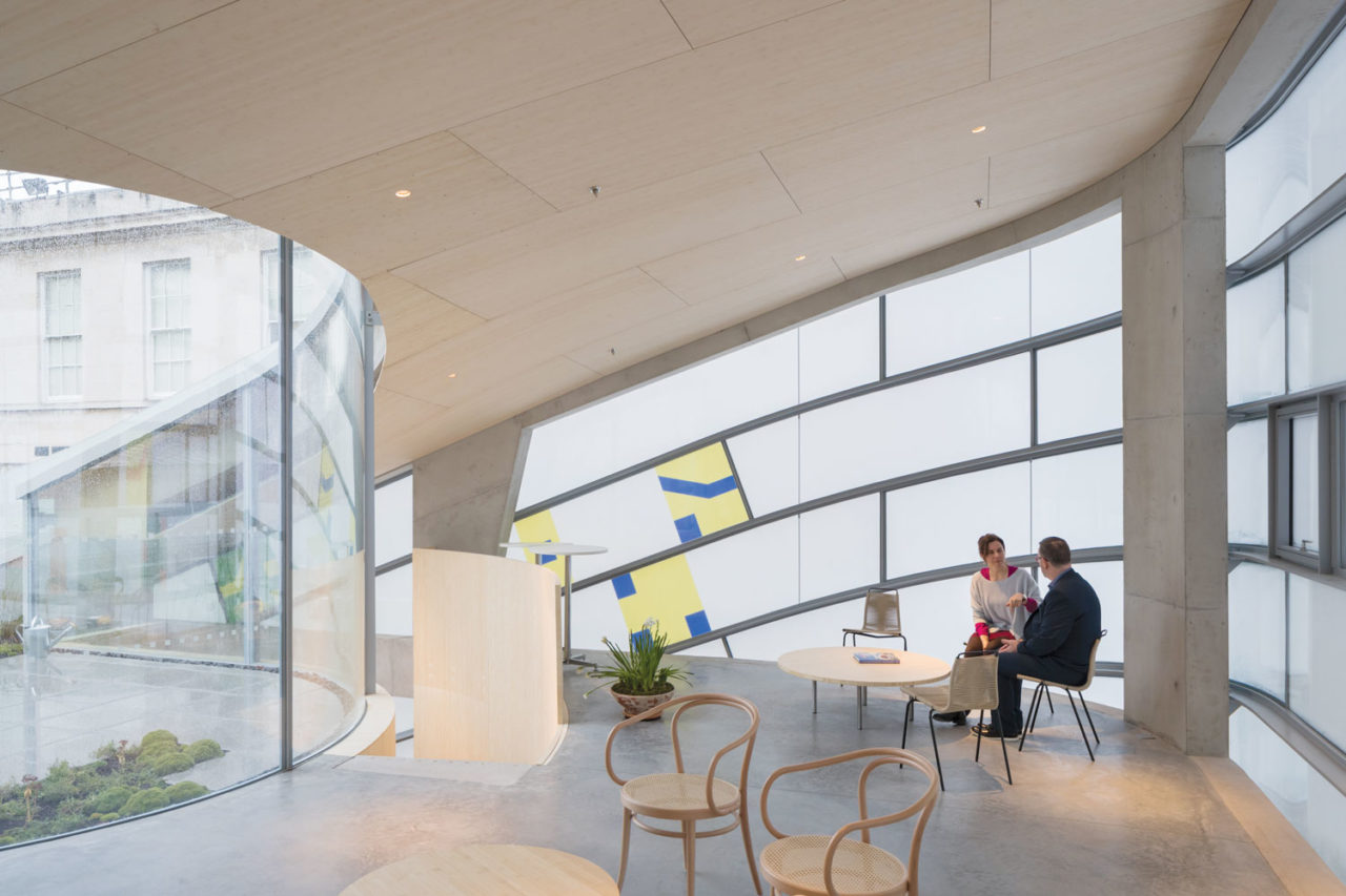 Steven Holl Architect's award-winning Maggie's Centre Bartsin London. Colored interior lighting plays with the translucent white glass of the façade to create a joyful, glowing atmosphere, while large windows provide views of an extended garden and an adjacent church. Photo: Iwan Baan.
