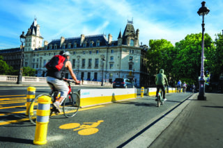 Cyclists biking over the Seine on newly minted protected bike lanes at Pont au Change in Paris. Plans for the “City of 15 Minutes”—or Ville du Quart d’Heure—were unveiled in January by Paris Mayor Anne Hidalgo’s reelection campaign, Paris en Commun. Image credit: Paris en Selle.