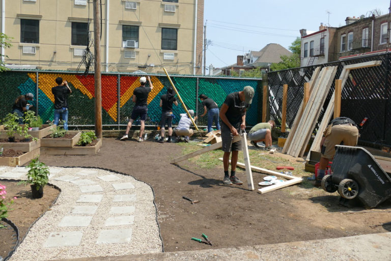 A photograph of a group of volunteers from Dattner Architects beginning to install a mural along the fence of the Services for the Underserved (S:US) urban garden during AIANY Day of Service.