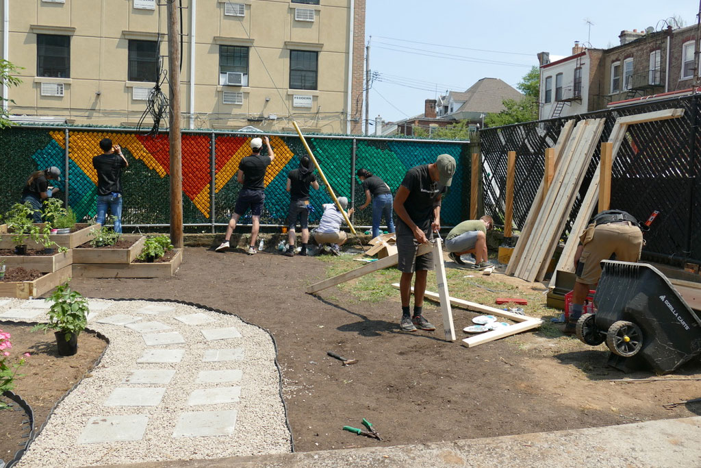 A photograph of a group of volunteers from Dattner Architects beginning to install a mural along the fence of the Services for the Underserved (S:US) urban garden during AIANY Day of Service.