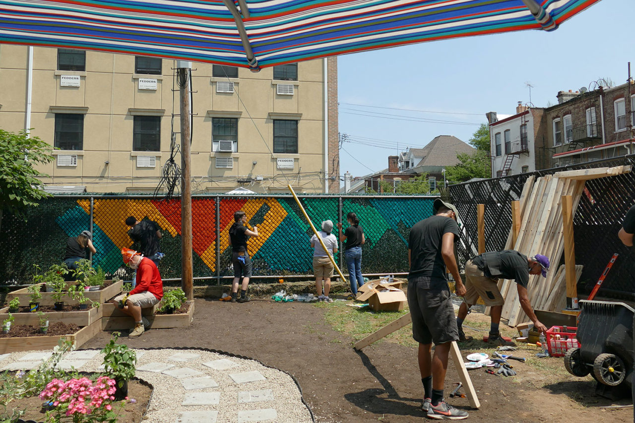 A photograph of a group of volunteers from Dattner Architects installing a mural along the fence of the Services for the Underserved (S:US) urban garden during AIANY Day of Service.