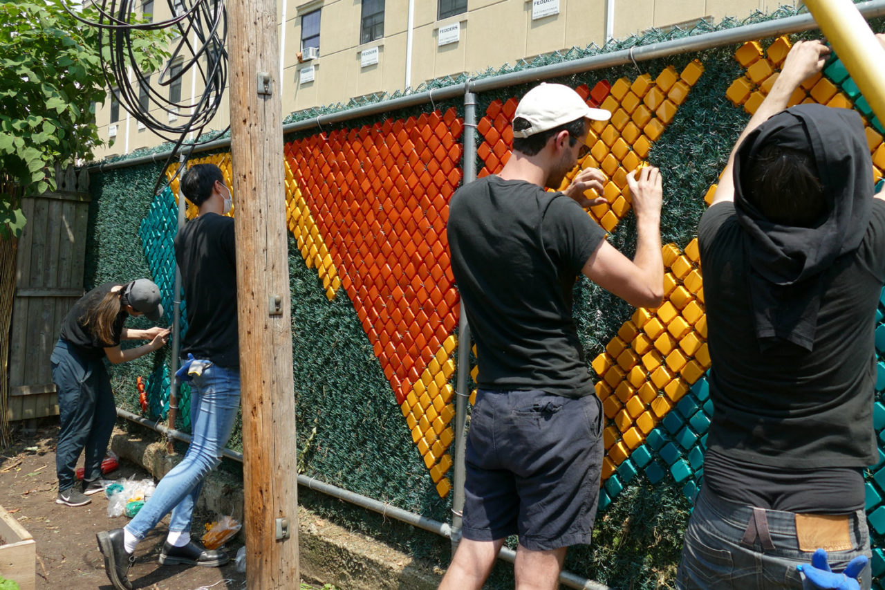 A photograph of 2 volunteers from Dattner Architects installing a mural along the fence of the Services for the Underserved (S:US) urban garden during AIANY Day of Service.