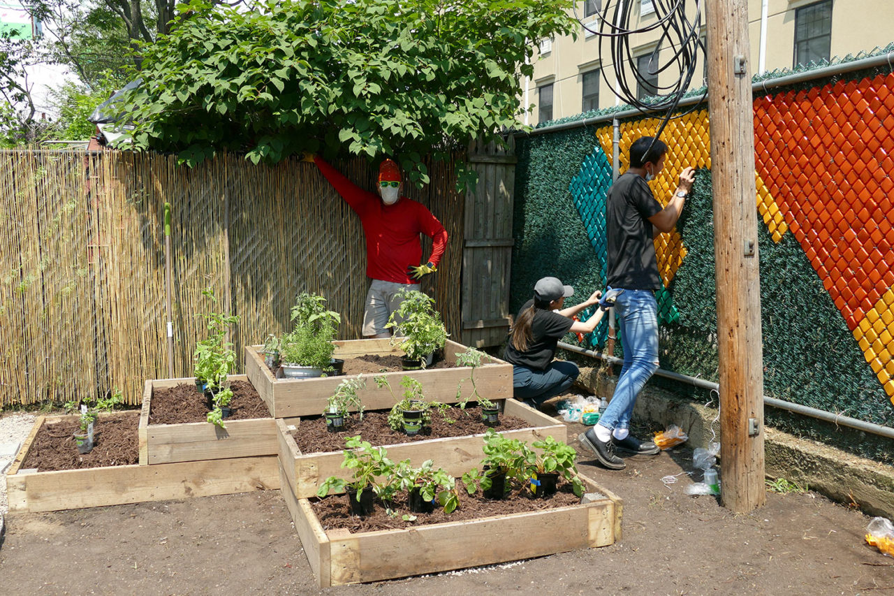 A photograph of 3 volunteers from Dattner Architects installing a mural along the fence of the Services for the Underserved (S:US) urban garden during AIANY Day of Service.