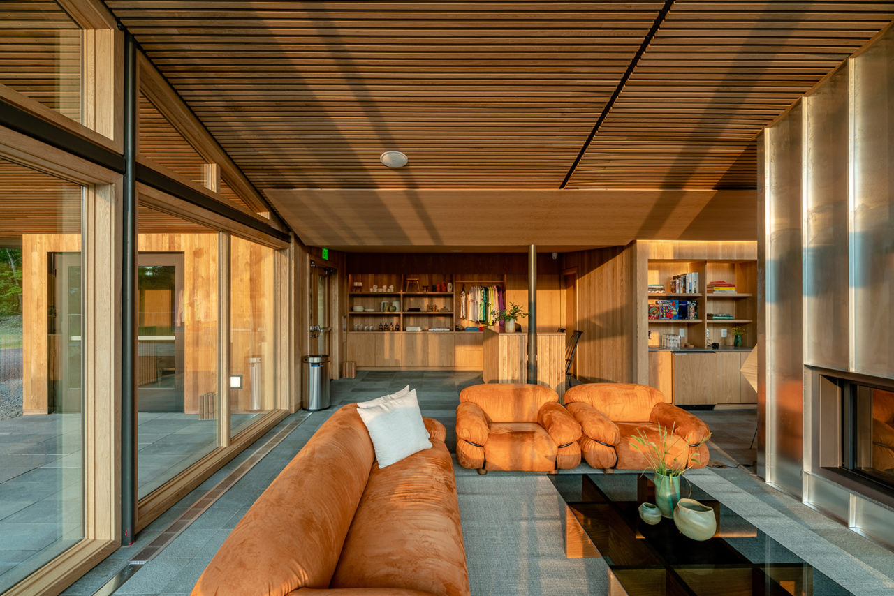 A photograph of the interior of Piaule Catskill's main house, depicting wooden ceilings, floor-to-ceiling glazing, and leather couches.