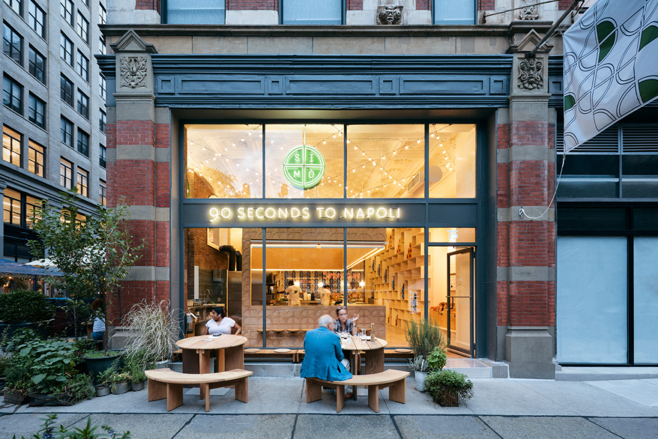 Photo of the exterior of SIMÒ pizza restaurant, with the interior lit up from the inside.