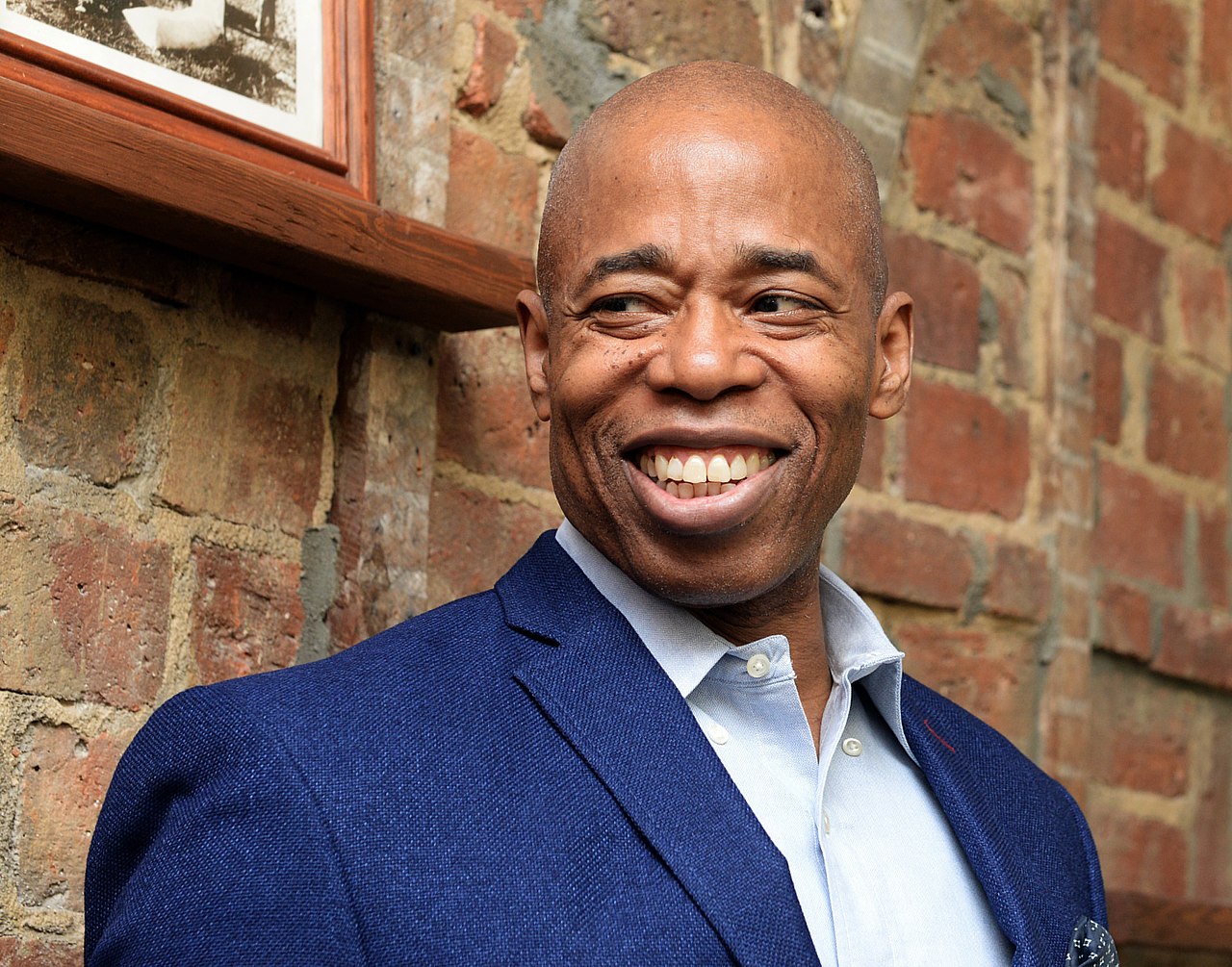 Photo of Eric Adams standing in front of a brick wall.