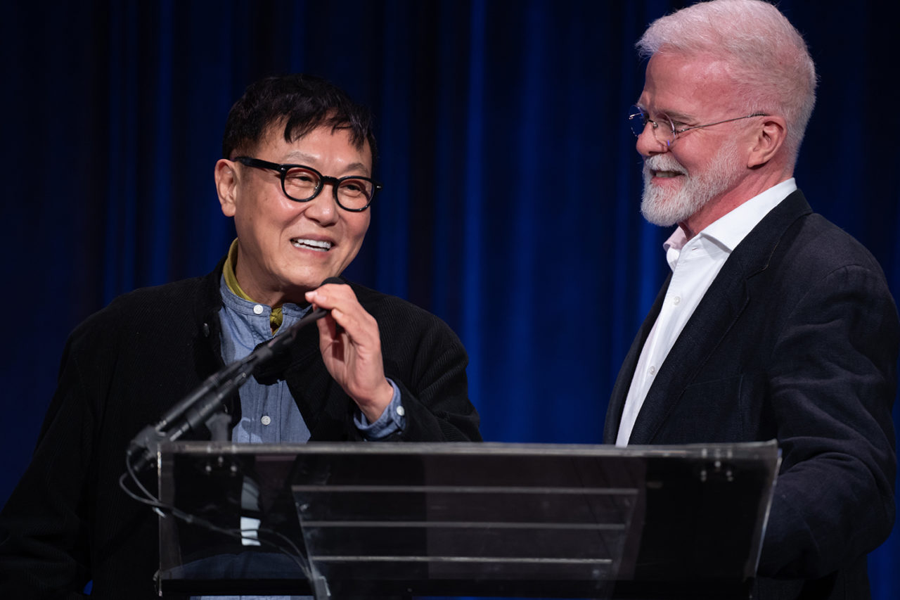Two men stand over a podium smiling at each other.