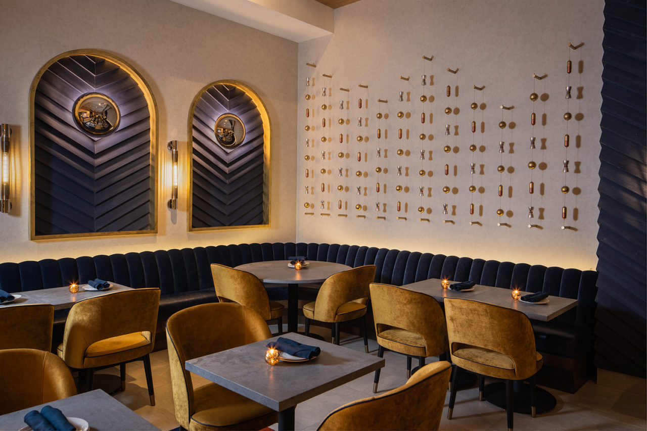 Restaurant interior featuring black tables with gold chairs and white walls with gold and midnight blue accents