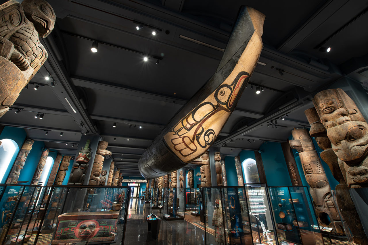 Exhibition hall featuring large, wood-carved artifacts and a dugout canoe suspended from the ceiling