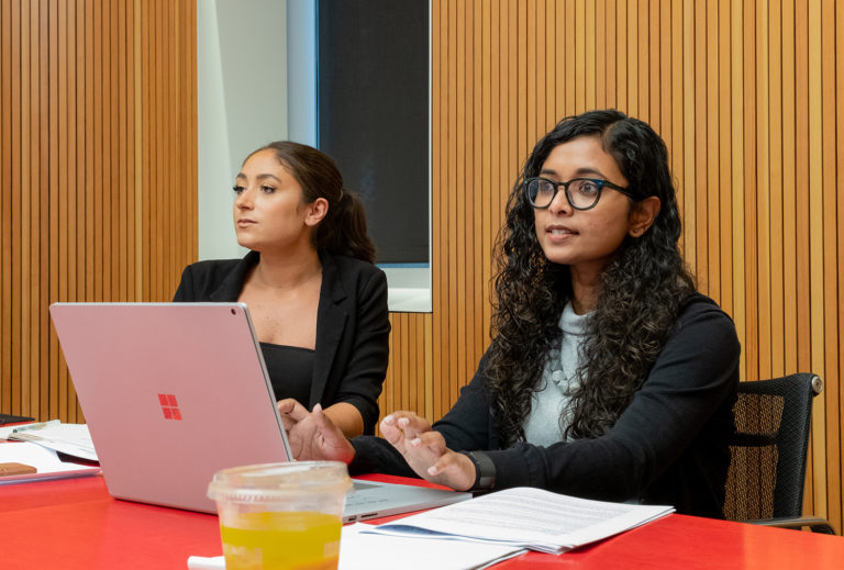 Two women sit at a red table in front of a computer