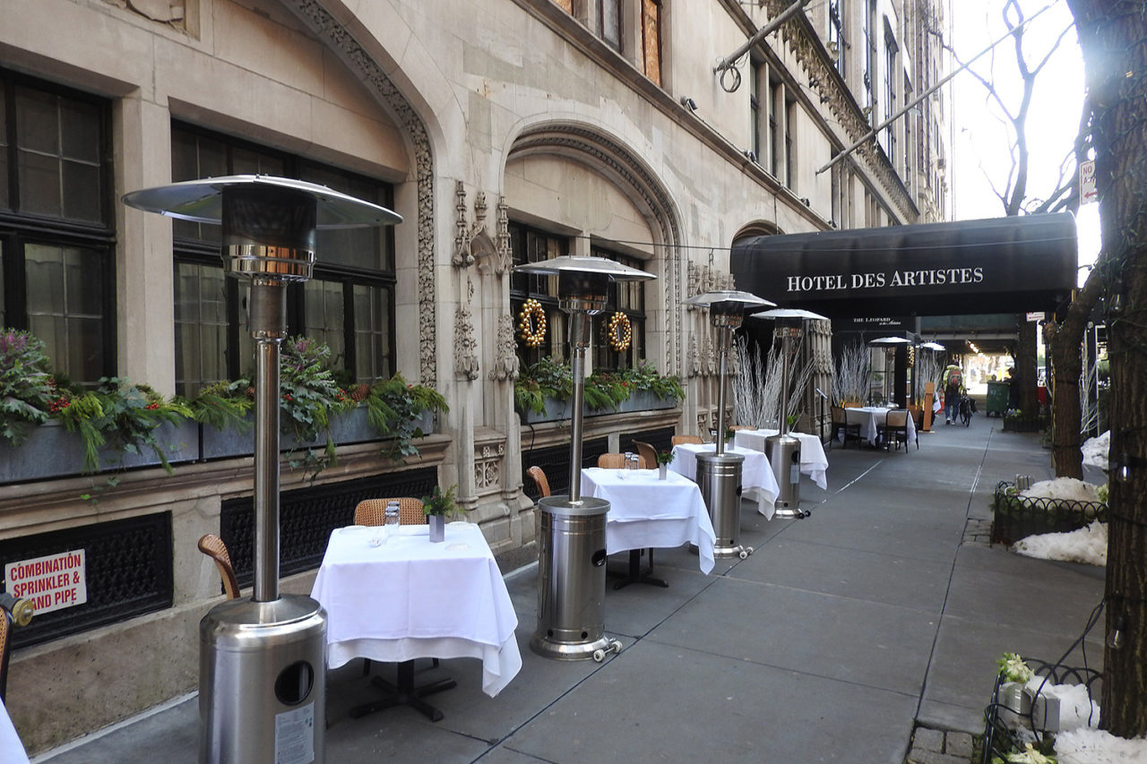 Dining tables with white tablecloths on a city sidewalk.