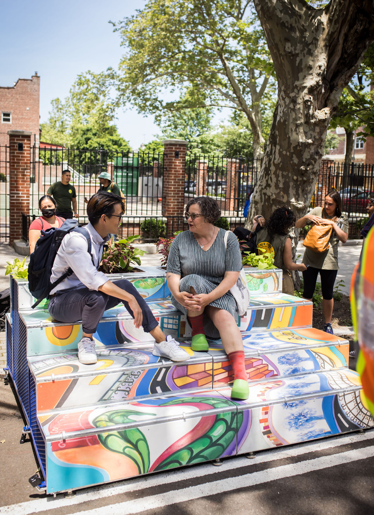 Two individuals chat while sitting on a colorful, stepped structure.