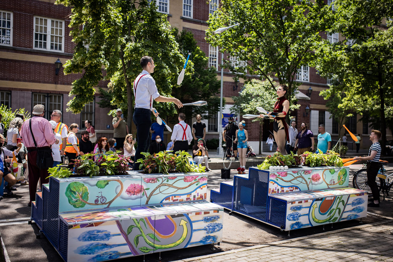 Two performers stand on stepped, colorful platforms placed on the street.