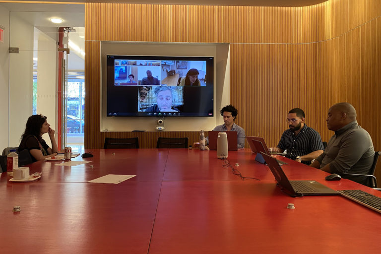 Four individuals sit around a red conference table