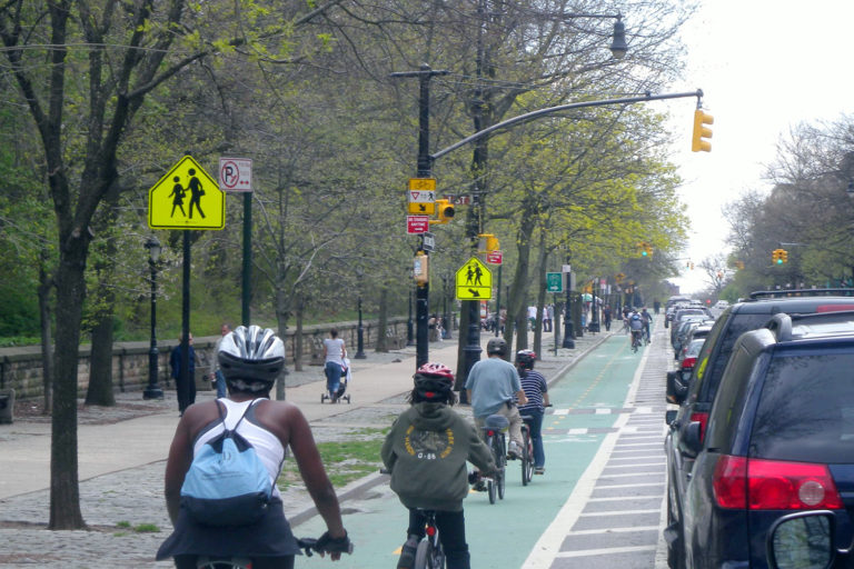 Several cyclists on a bike lane adjacent to a park