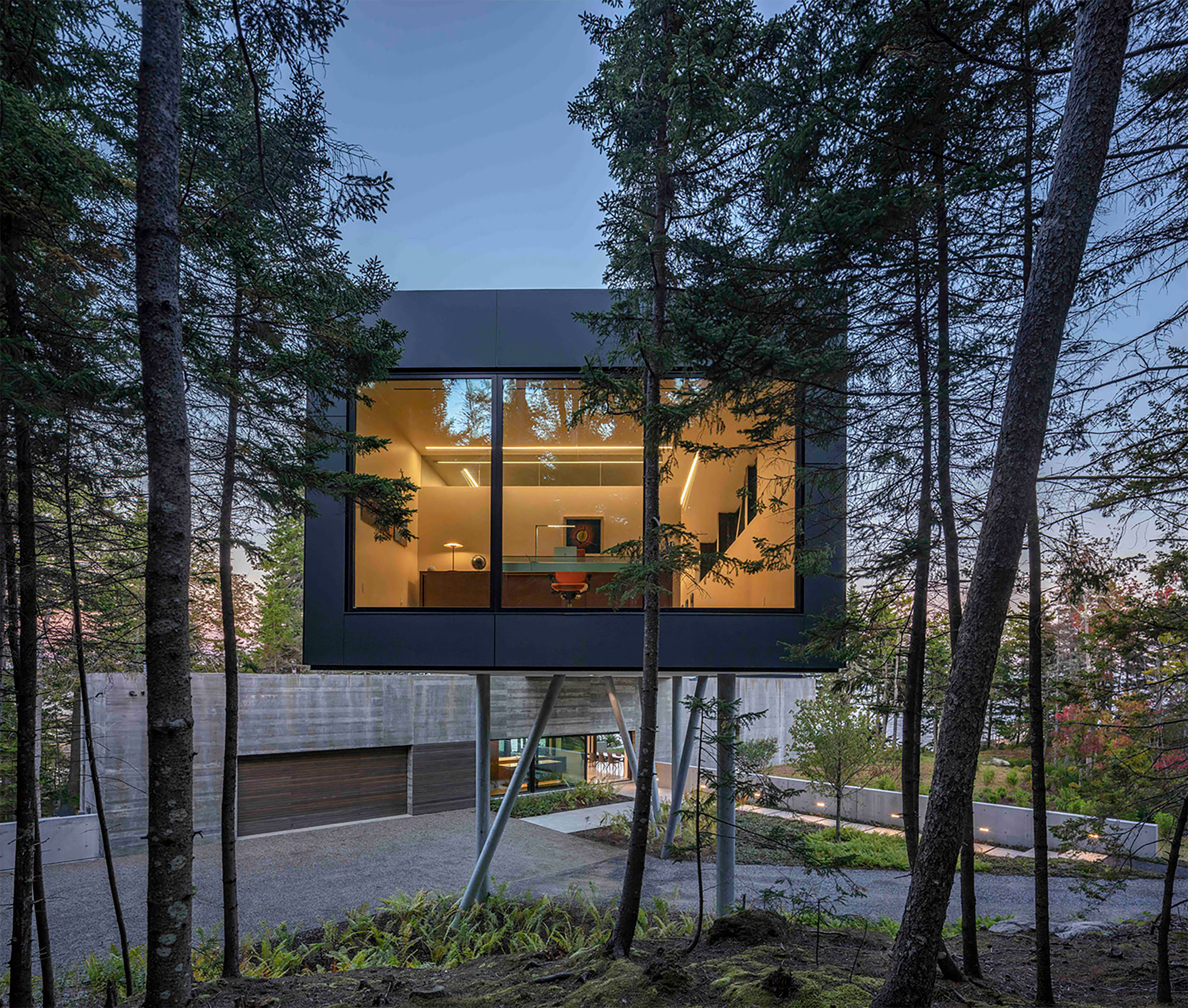 A wing of a modern house juts into the trees and appears as though suspended over another volume of the house