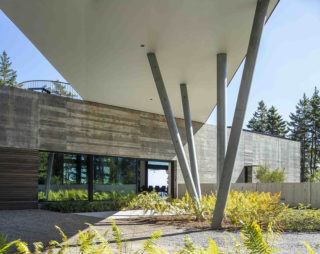 The exterior of a structure with four angled columns supporting a cantilevered structure above it