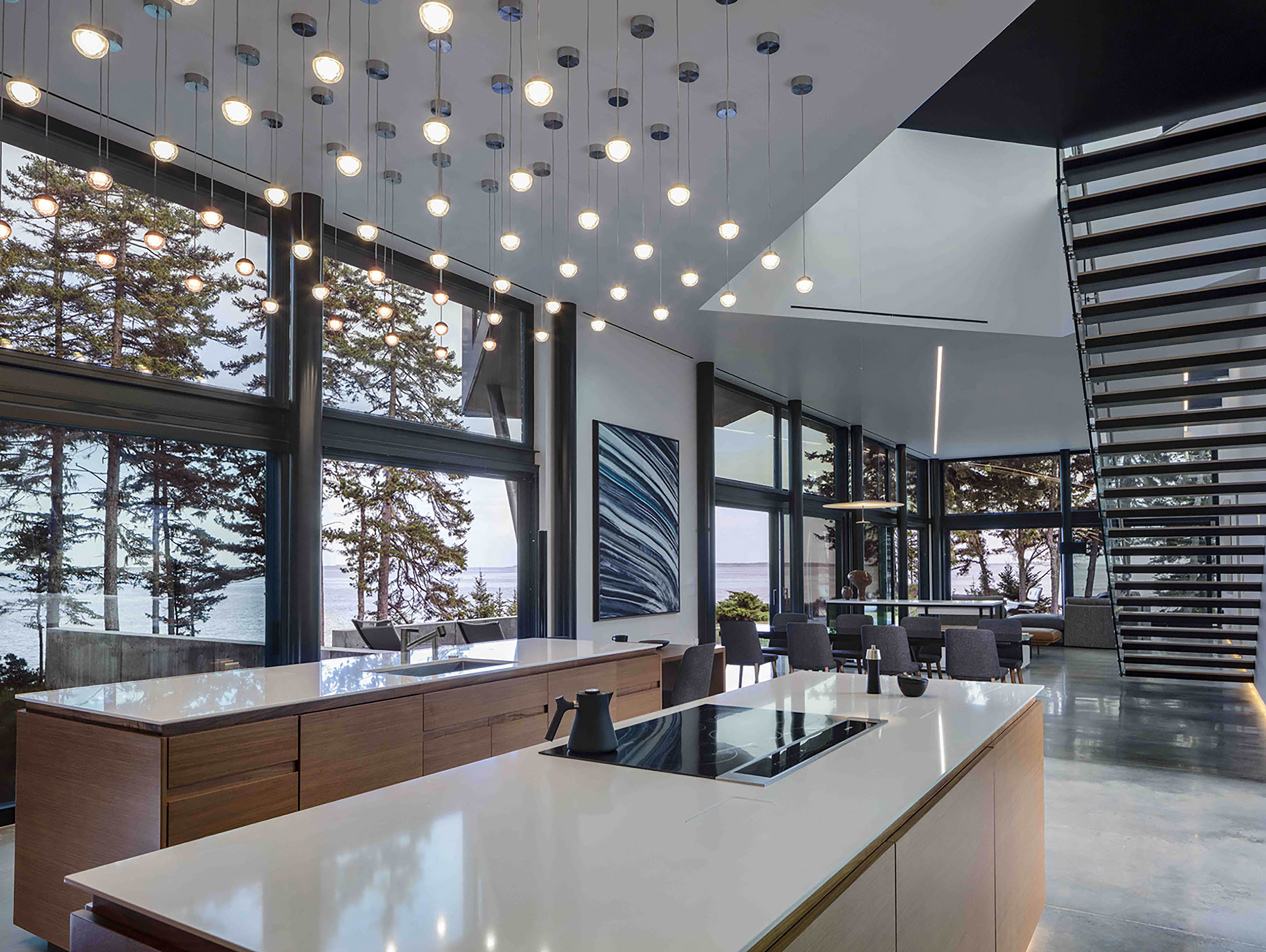 A modern open kitchen interior looking out at a dining area and glass walls with a view to water