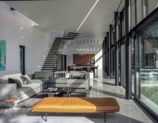 A modern house interior with a chaise lounge in brown leather, beside a sofa, in the foreground and a floating staircase in the background