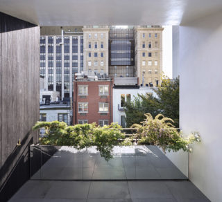 An apartment balcony with a large steel planter filled with plants. In the background, more apartment buildings can be seen.