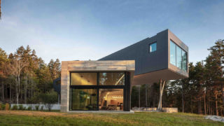 The exterior of a house with large glass windows and a cantilevered volume in the rear