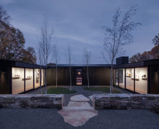 The inner courtyard of a modern house with gravel and stone benches, surrounded by glass walls that are illuminated by the house interiors