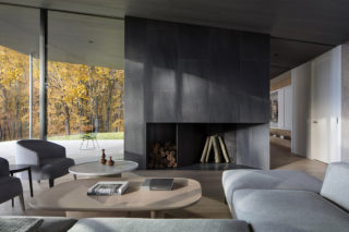 A modern living room with a large fireplace, wooden coffee table, and edge of a gray sofa