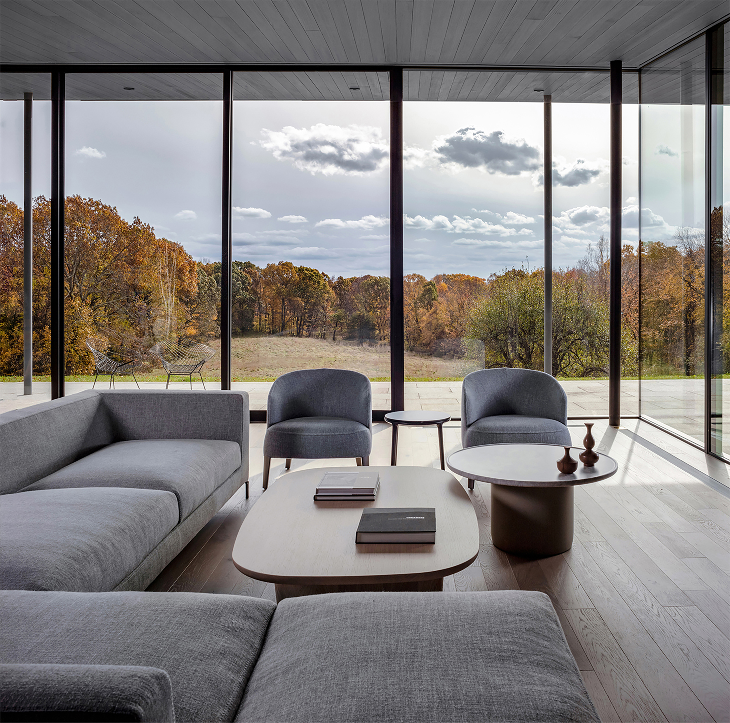 A modern living room with glass walls looking out on a fall country landscape with changing leaves