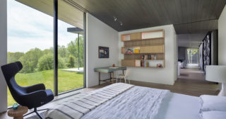 A modern bedroom with white and striped bed linens in the foreground and a door looking out on the outside with a green patch of grass