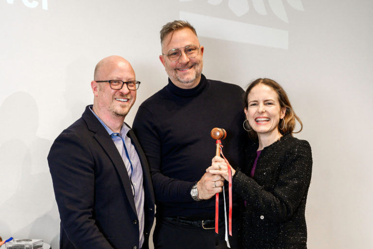 A man with glasses stands next to a man and a woman who each hold a gavel with a ribbon.