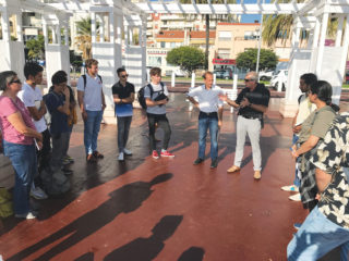 A group of people standing around in a circle and one person speaking to the group