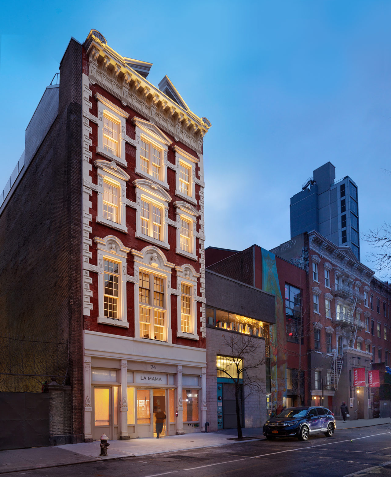 Exterior view of four-story brick building at dusk lit from within