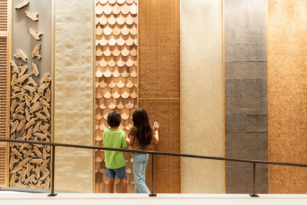 Two children stand in front of a wall with vertical panels of different wood surfaces.
