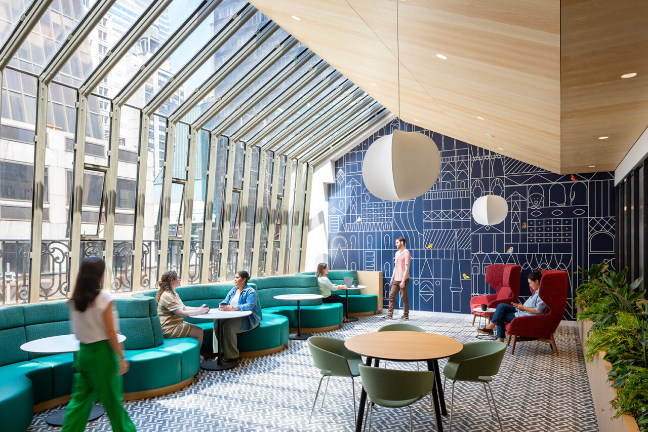 People standing and sitting around in an airy dining/meeting area with glass windows and soft booths.