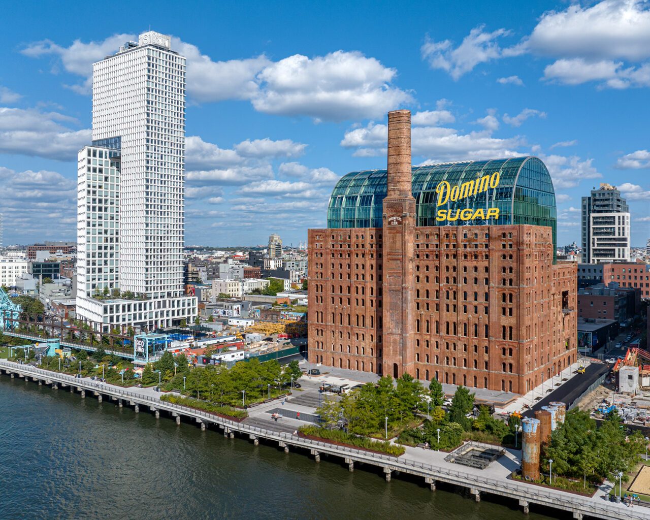 The redesigned Domino Sugar Factory building stands against the waterfront and sky.