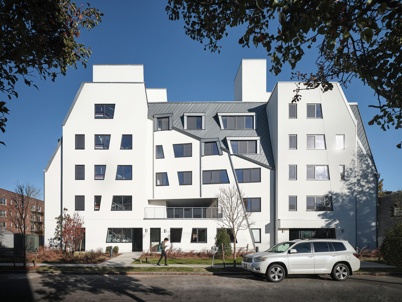 A white apartment complex with an asymmetric, geometric outline and a variety of window shapes.