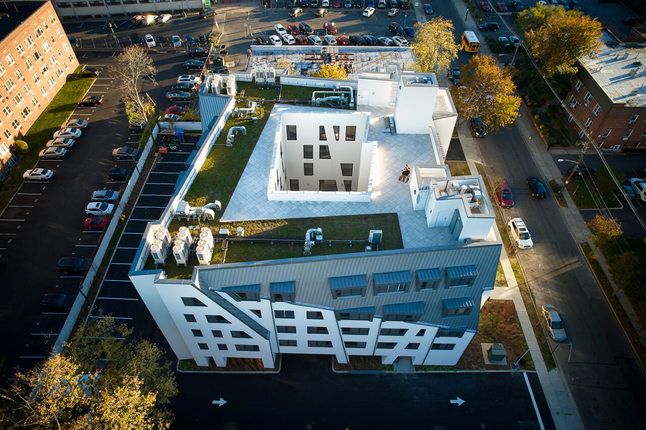 A bird's-eye view of the Allan & Geraldine senior living apartment complex, with a landscaped rooftop. Cars are parked in the lot beside it.