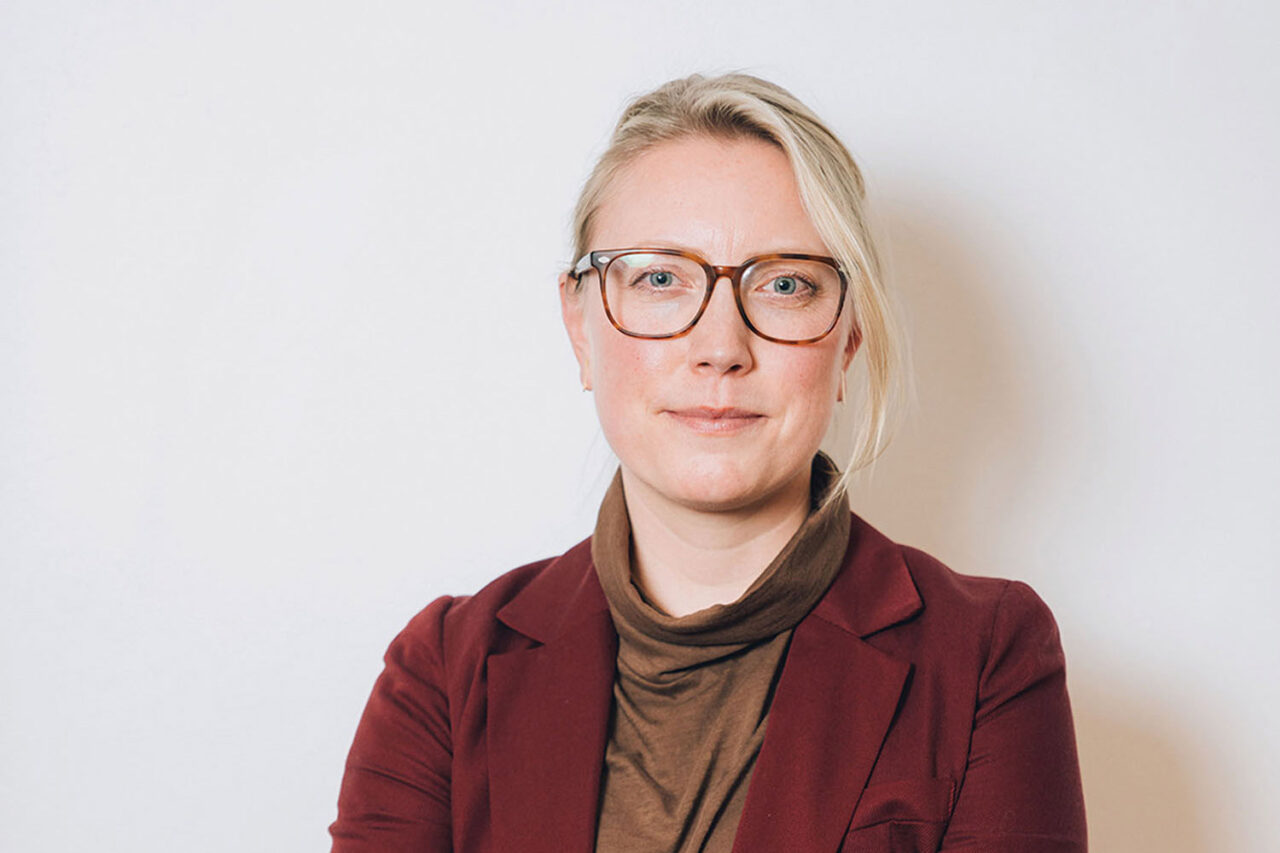 Headshot of Jennifer Krichels wearing glasses and a burgundy blazer against a white background