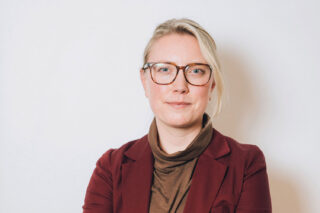 Headshot of Jennifer Krichels wearing glasses and a burgundy blazer against a white background