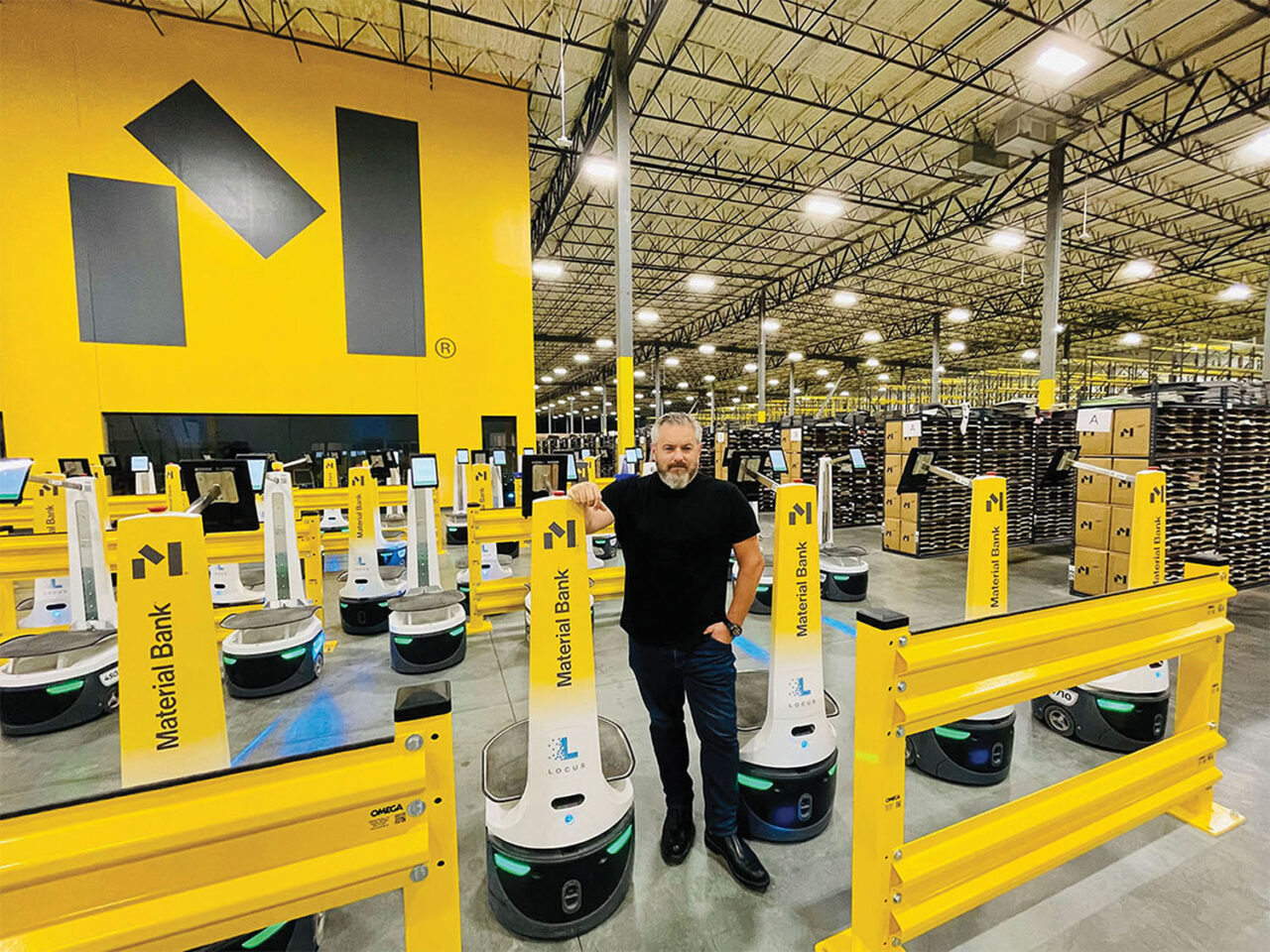 Adam Sandow, chairman and CEO of Material Bank, poses with robots that help perform some of the material sample fulfillment at the company’s logistics hub in Memphis, TN.