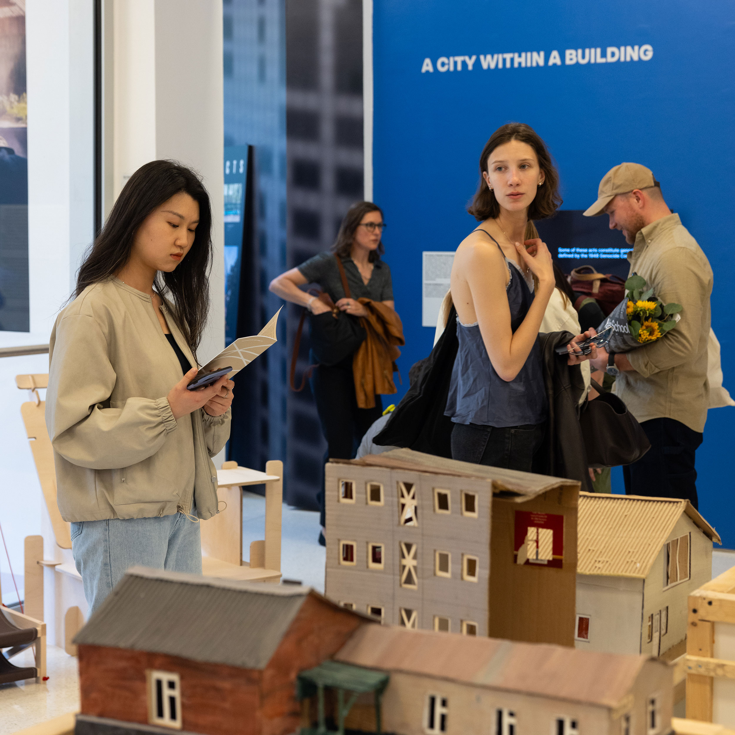Interior of Center for Architecture gallery with people looking at models and wall text for an exhibition