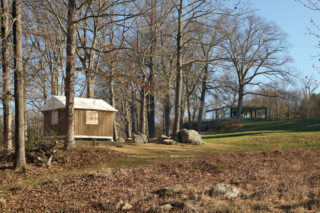 A photo of Shigeru Ban's Paper Log House amongst the woodsy landscape at The Glass House.