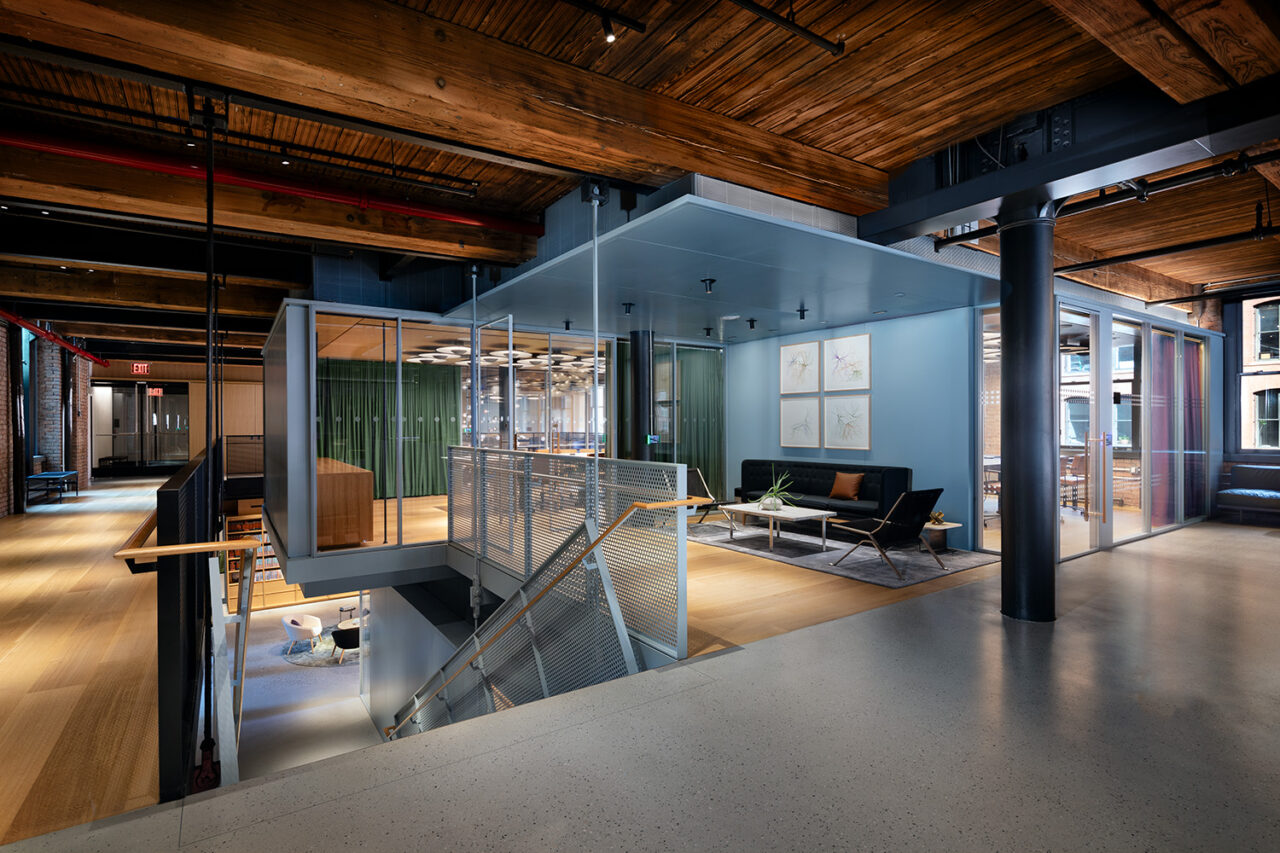 An open-air interior office scene with a stairwell at the left and different rooms at the right.