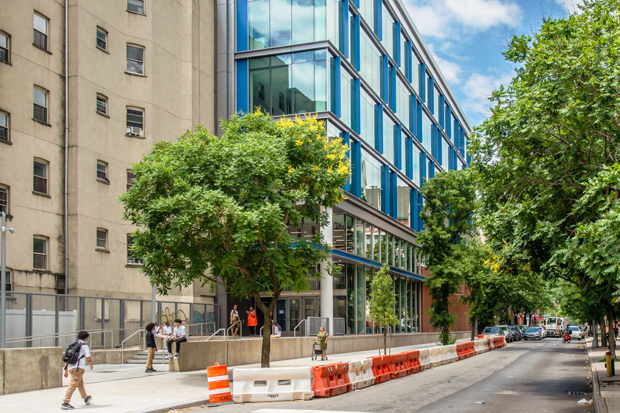 An exterior shot of the East Harlem Scholars Academy High School, with trees out front and passersby.