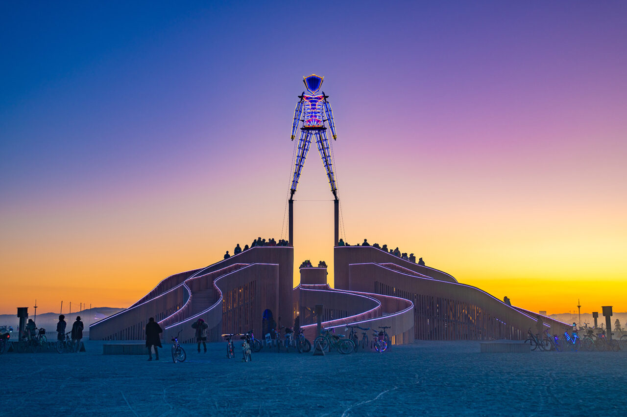 A sunset photo of the skeletal structure standing atop the building in the desert.