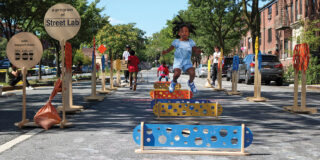 A scene of a child jumping over a hurdle, and other kids playing in the street.