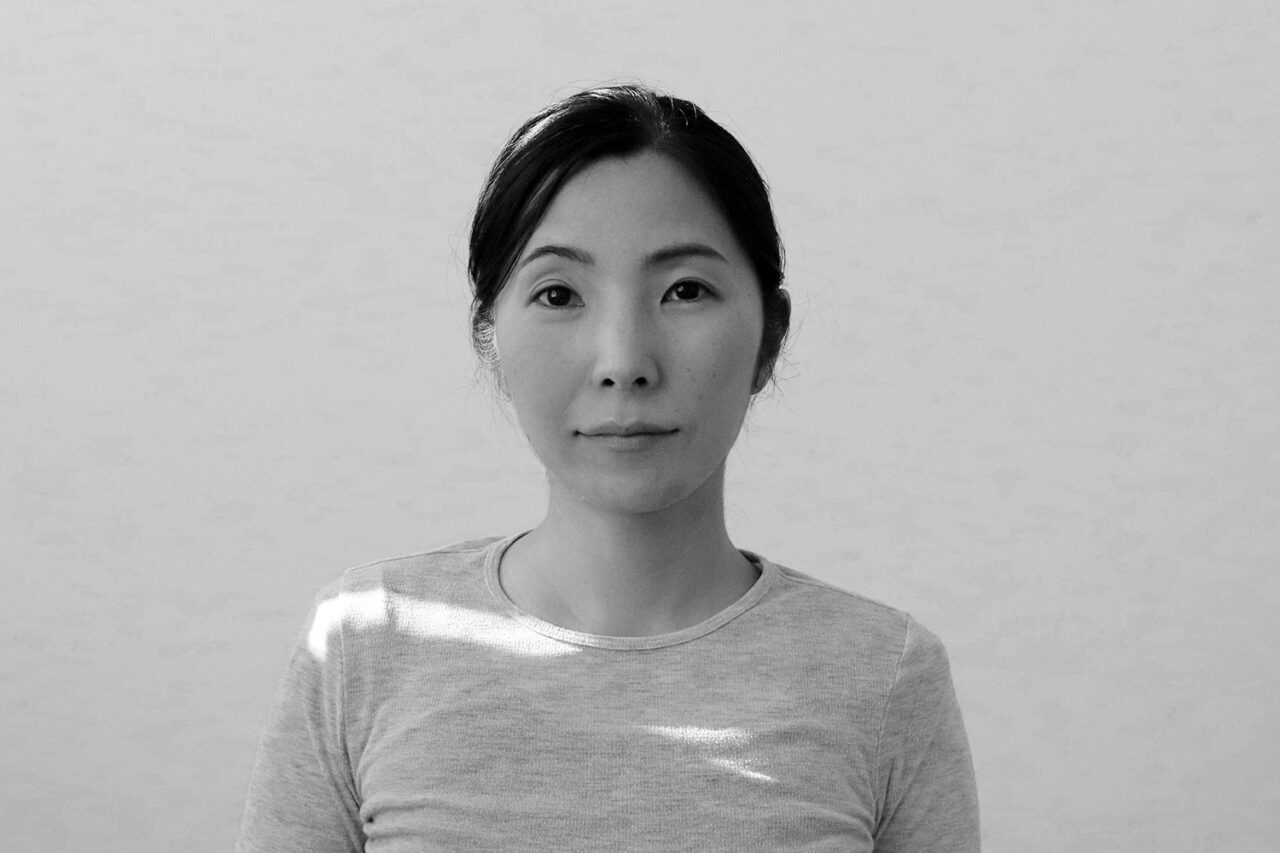 Black and white headshot of a Japanese woman with dark hair tied back.