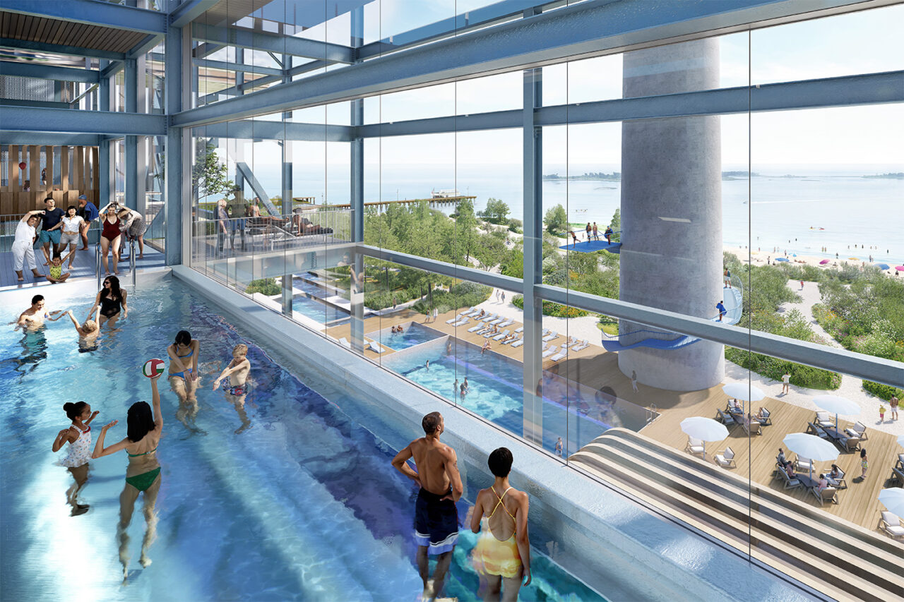 People in a pool look out onto the below pool deck and the outstretched beach.