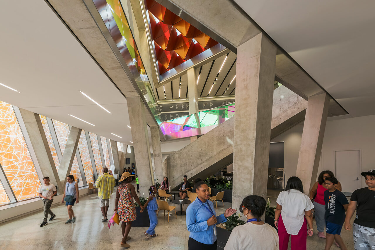 Interior shot of the central atrium with people bustling about. Colorful dichroic windows in the background.