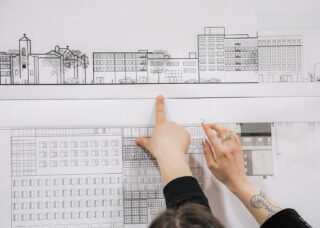 Hands pointing to a blueprint of buildings.